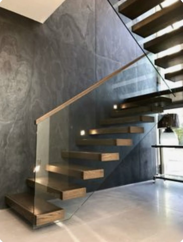 a stair case with glass railing and wooden steps next to a wall mounted light fixture