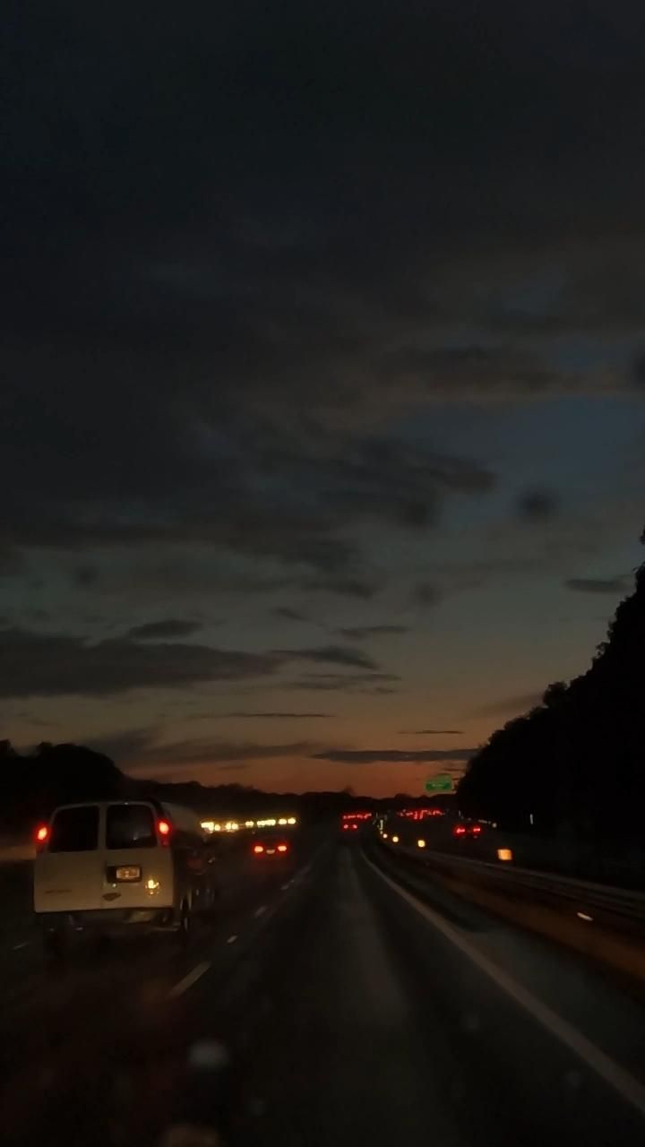 a car is driving down the highway at night with its lights on and dark clouds in the sky