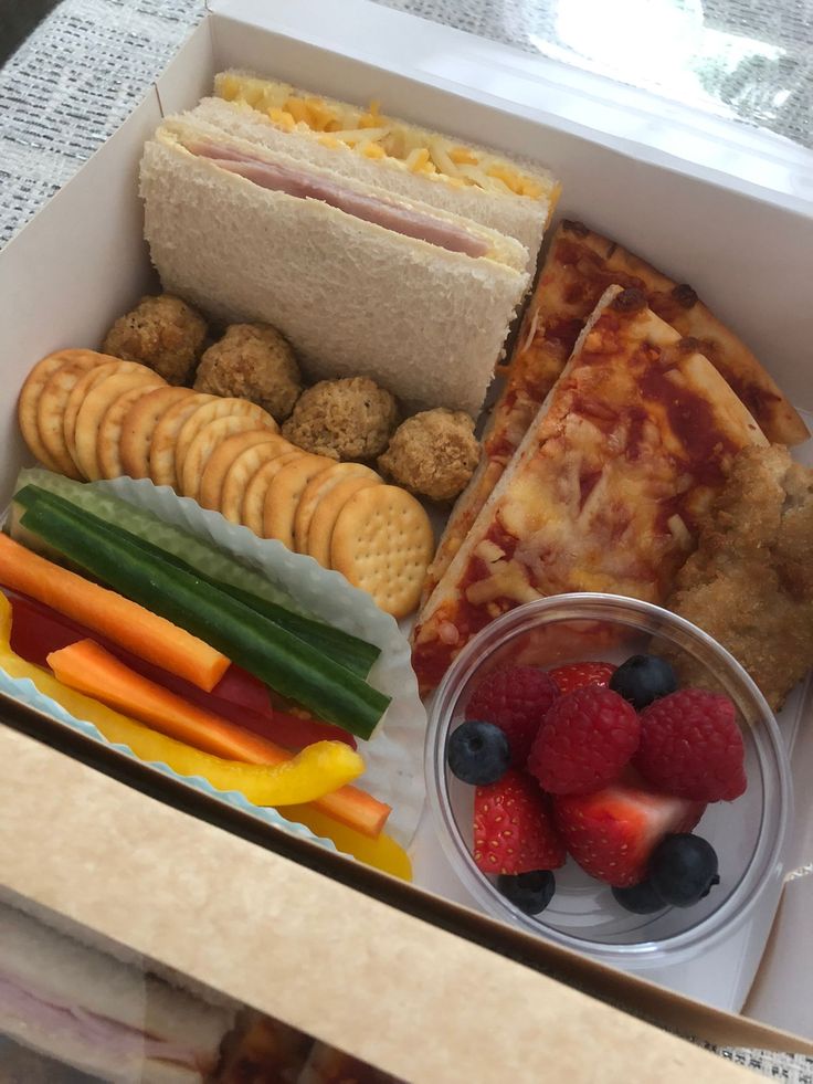 a box filled with different types of food next to crackers and fruit on top of a table