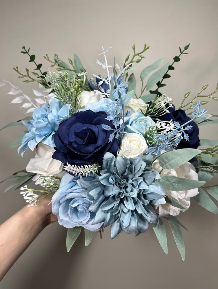 a bouquet of blue and white flowers is held by someone's hand in front of a gray wall