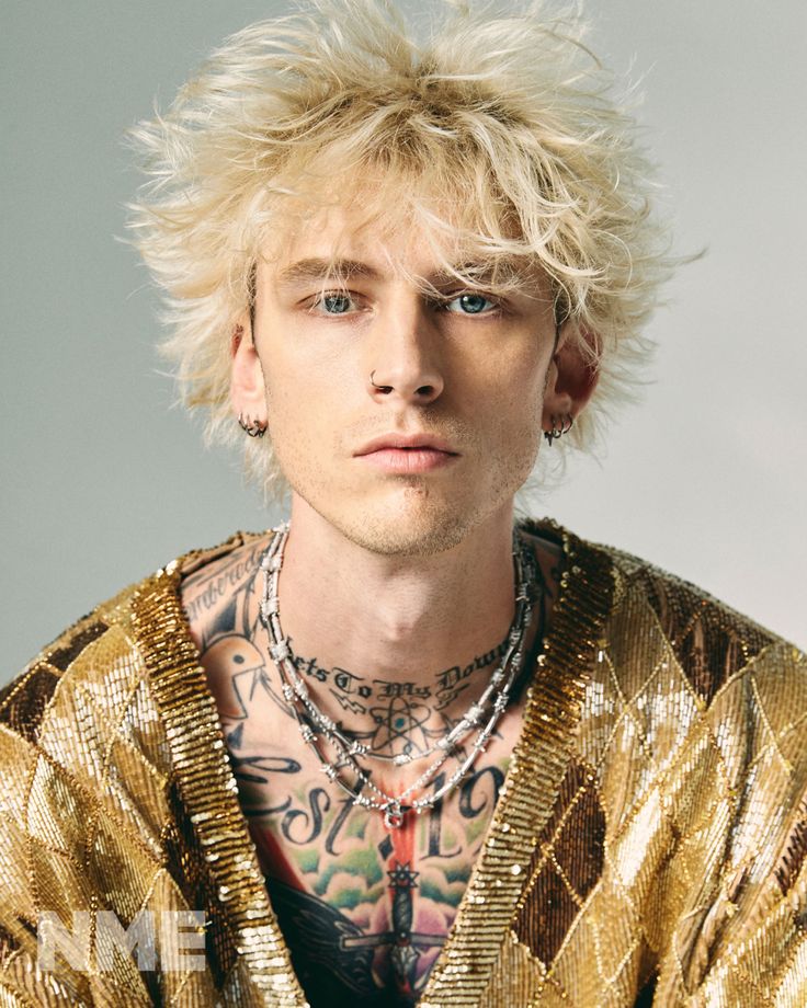 a man with blonde hair and piercings wearing a gold jacket looking at the camera