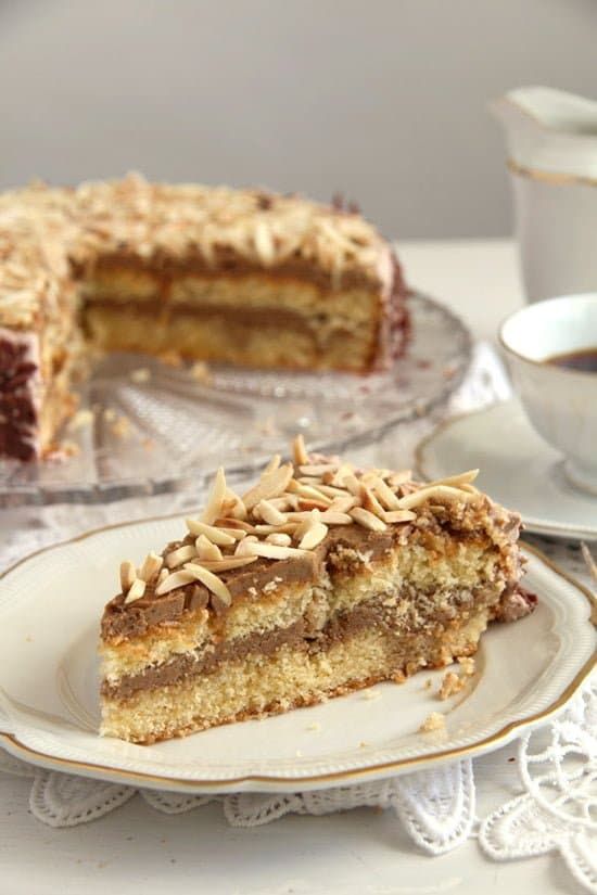 a piece of cake on a plate with a cup of coffee in front of it