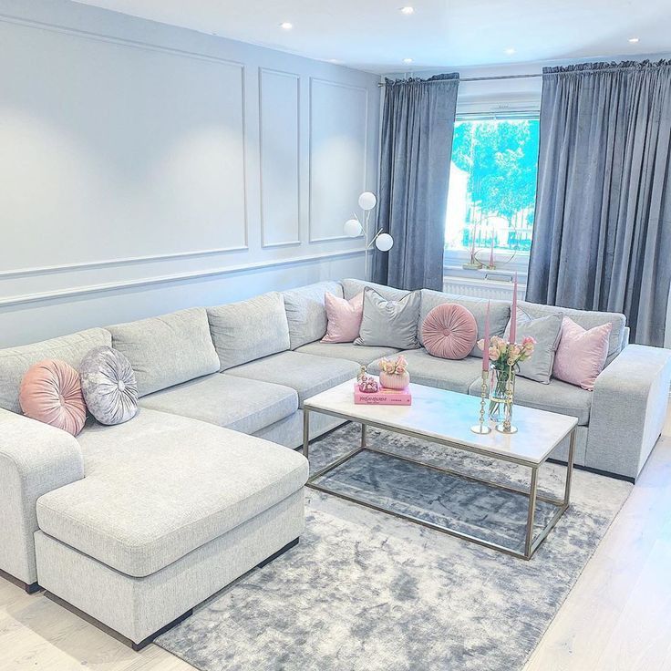 a living room with gray couches and pink pillows on top of the sectional sofa