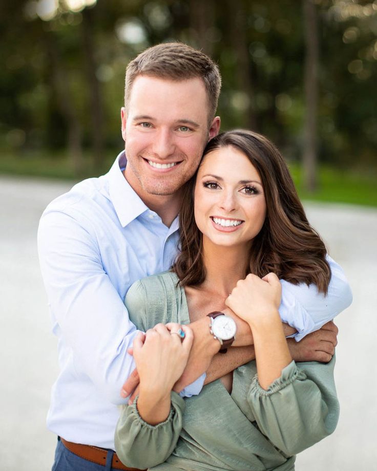 a man and woman hugging each other in front of the camera with trees in the background