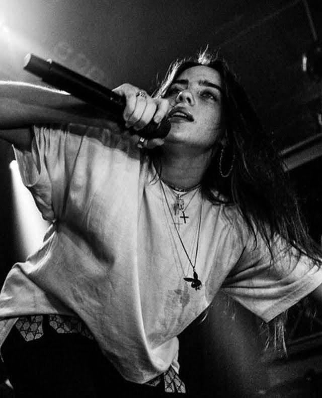 black and white photograph of a woman holding a microphone up to her ear while performing on stage