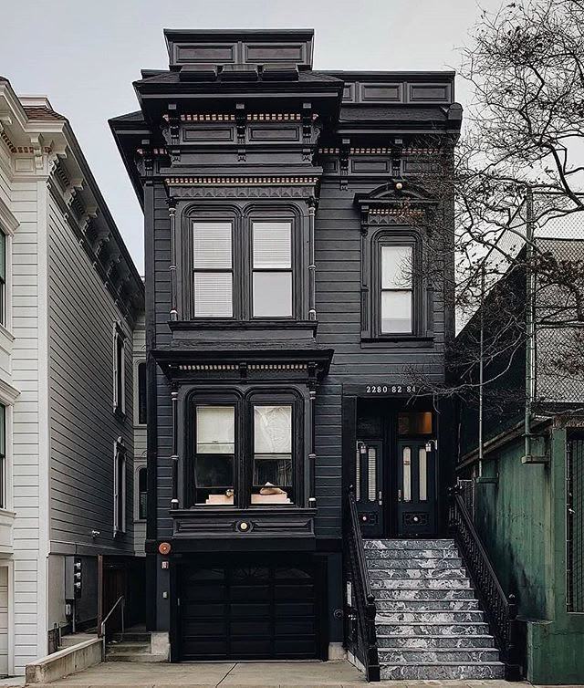 an old black house with stairs leading up to the front door and two story building