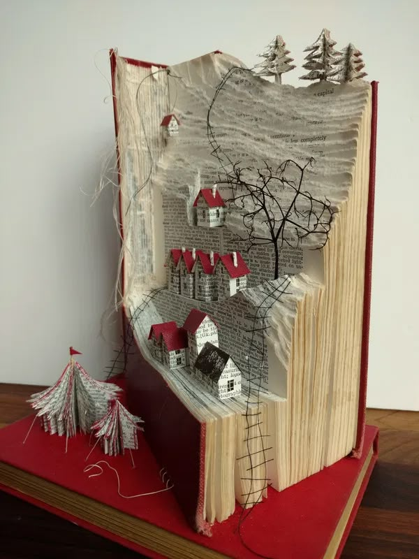 an open book with paper houses and trees on it, sitting on top of a wooden table