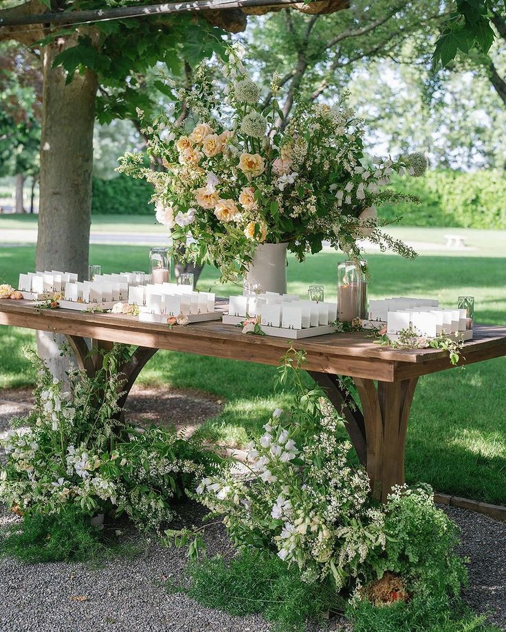 a wooden table with candles and flowers on it in front of a large green tree