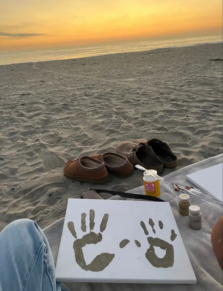 someone's hand and foot prints are on the sand at the beach as the sun sets