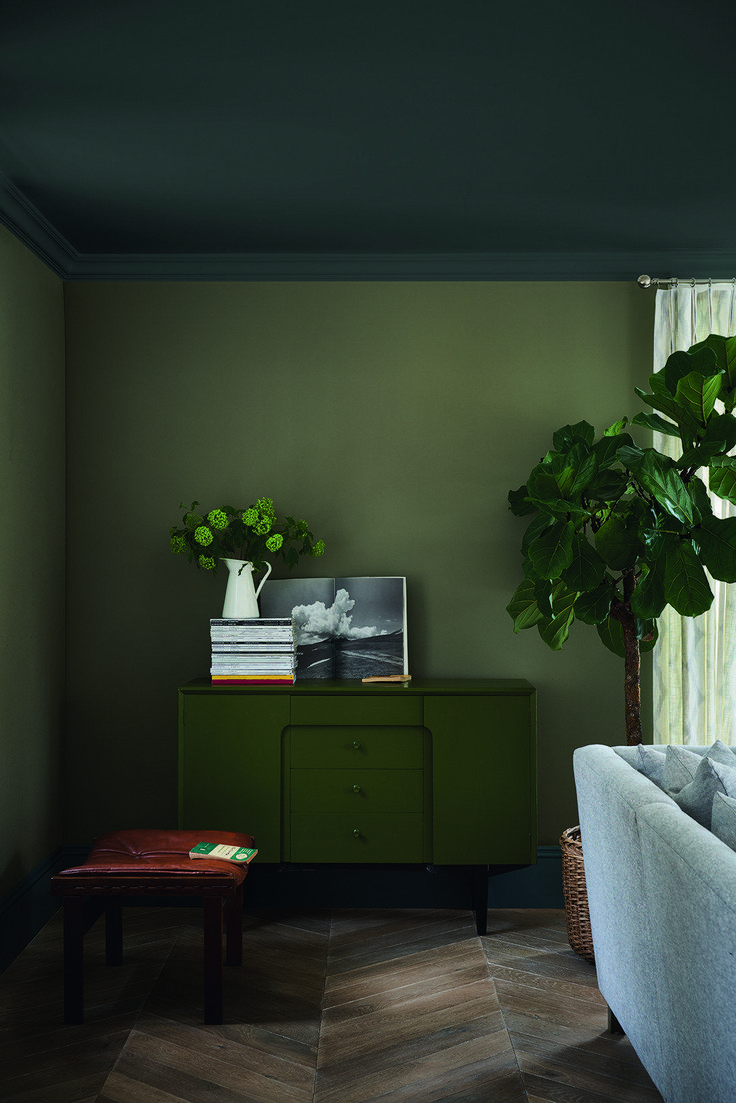 a living room with green walls and a plant on top of a dresser next to a window