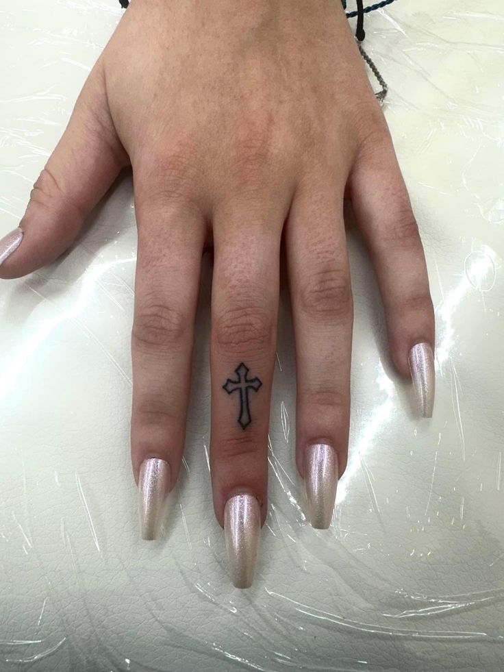 a woman's hand with a small cross tattoo on her left thumb and ring finger