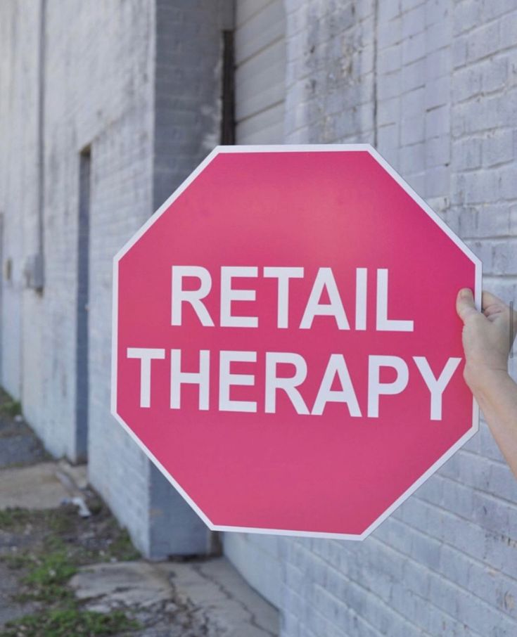 a person holding up a red stop sign that says retail therapy on the side of a building