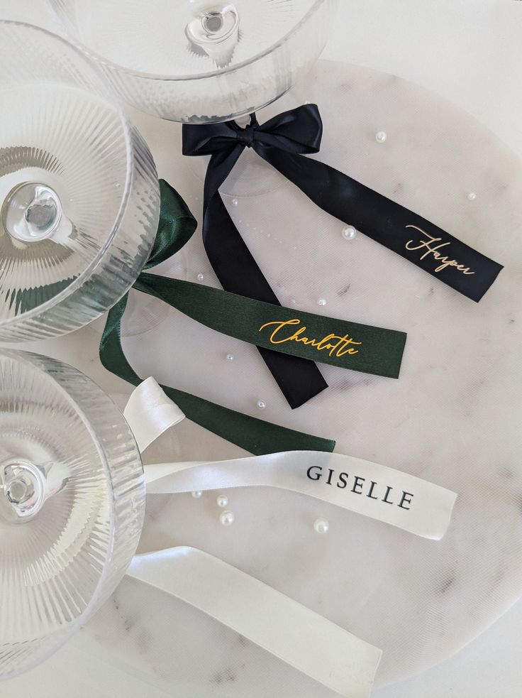 three wine glasses are sitting next to each other on a marble platter with ribbon and name tags