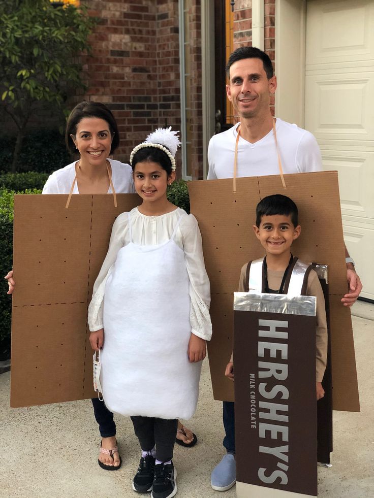 three people standing in front of a house with cardboard signs on their heads and two children holding paper bags behind them