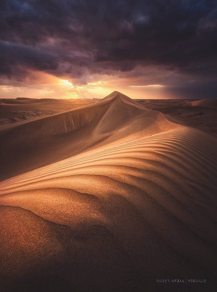 the sun shines through dark clouds over sand dunes