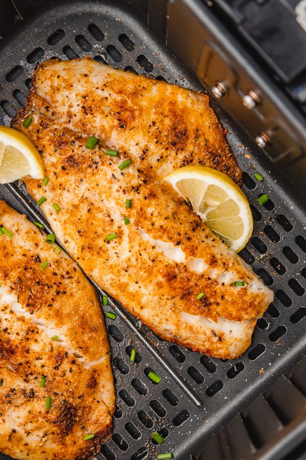 two pieces of chicken on a grill with lemon wedges