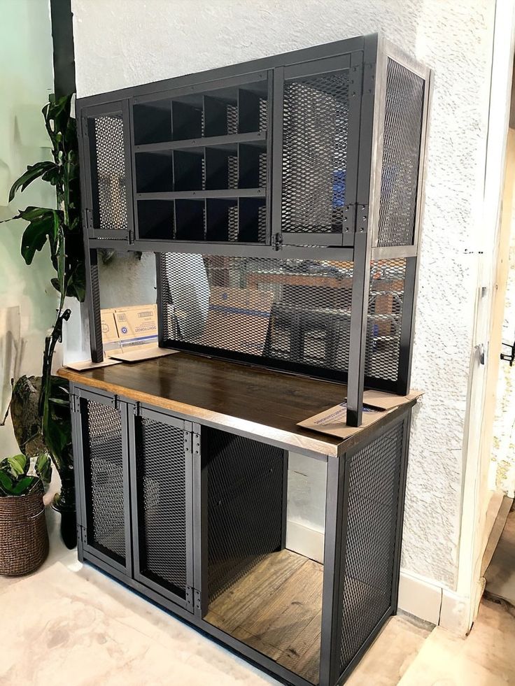 an office desk with metal mesh doors and shelves on the wall next to a potted plant