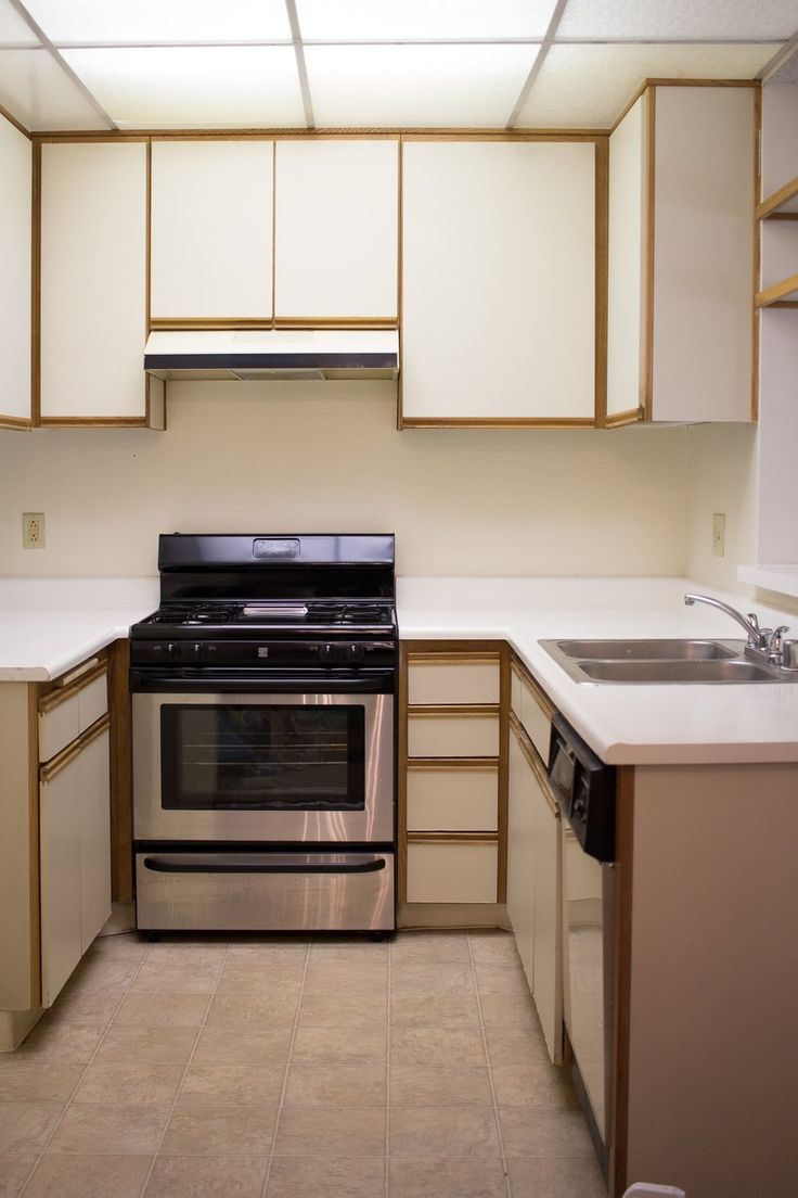 an empty kitchen with white counter tops and black stove top oven in the corner,