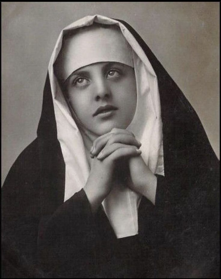 an old black and white photo of a woman wearing a nun outfit with her hands on her chest