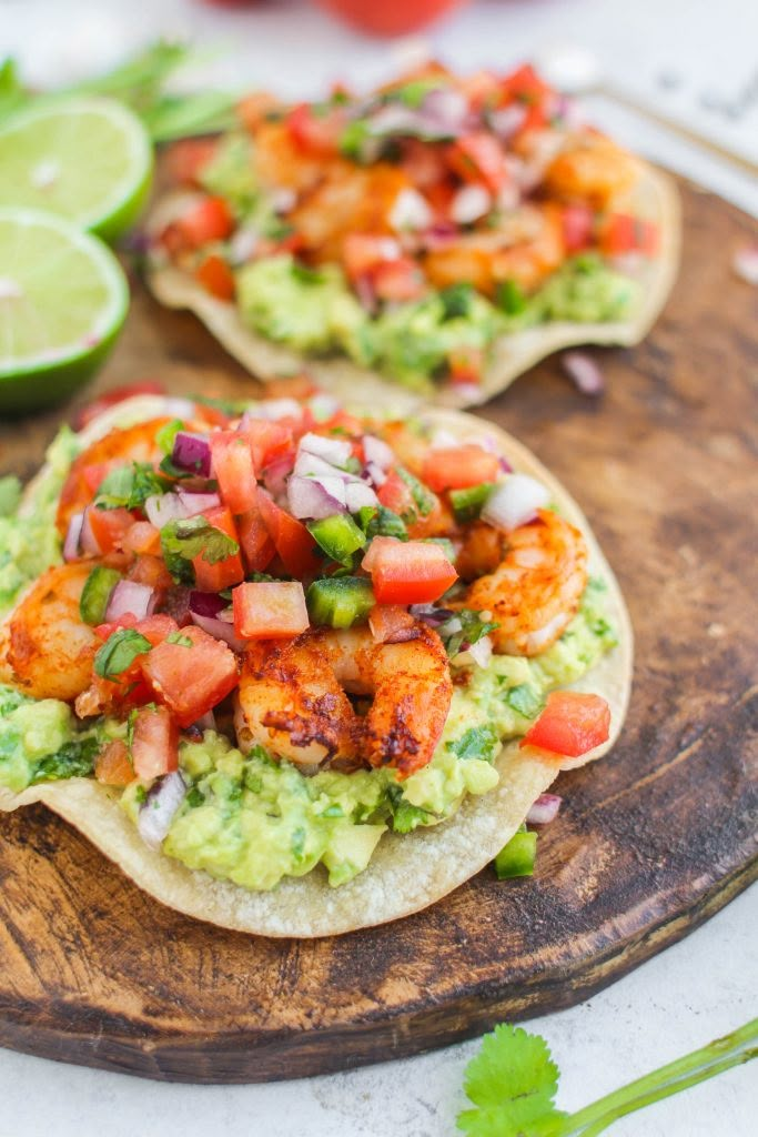 two tortillas with shrimp and guacamole on a wooden cutting board