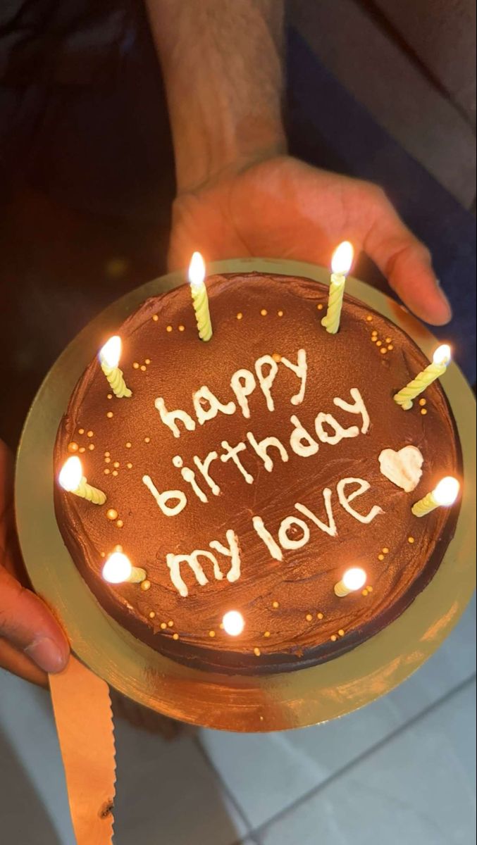 a person holding a cake with lit candles on it that says happy birthday my love