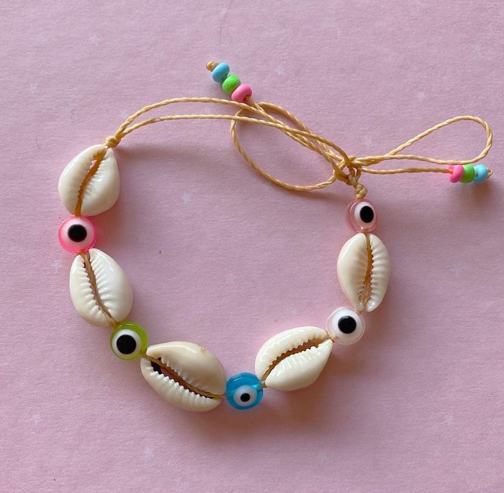 a bracelet made out of seashells and beads on a pink surface with string