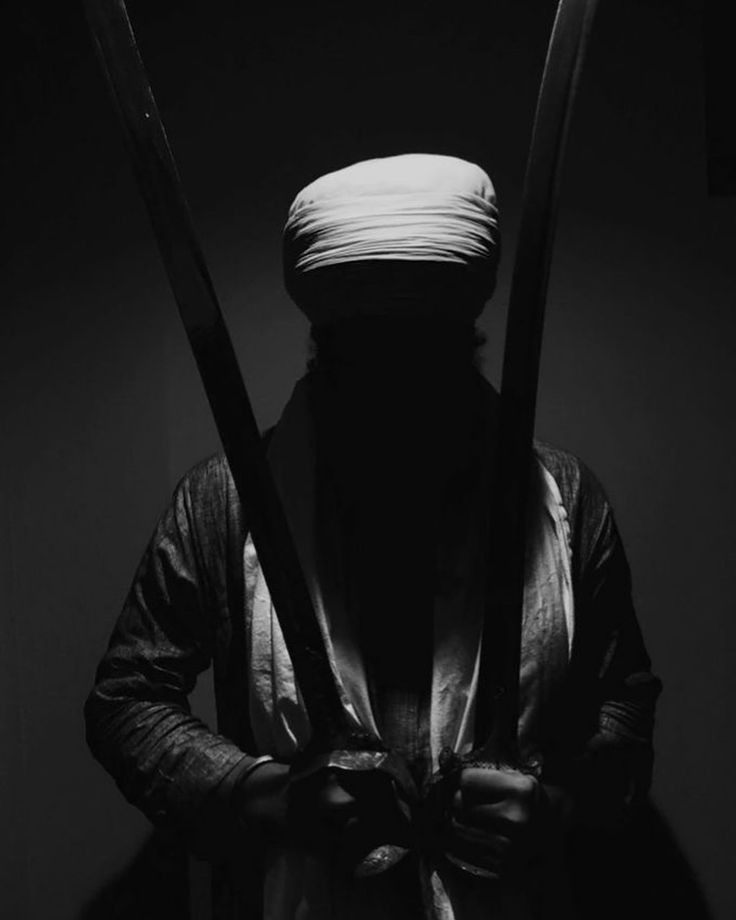 black and white photograph of a man with two swords in his hands, wearing a turban