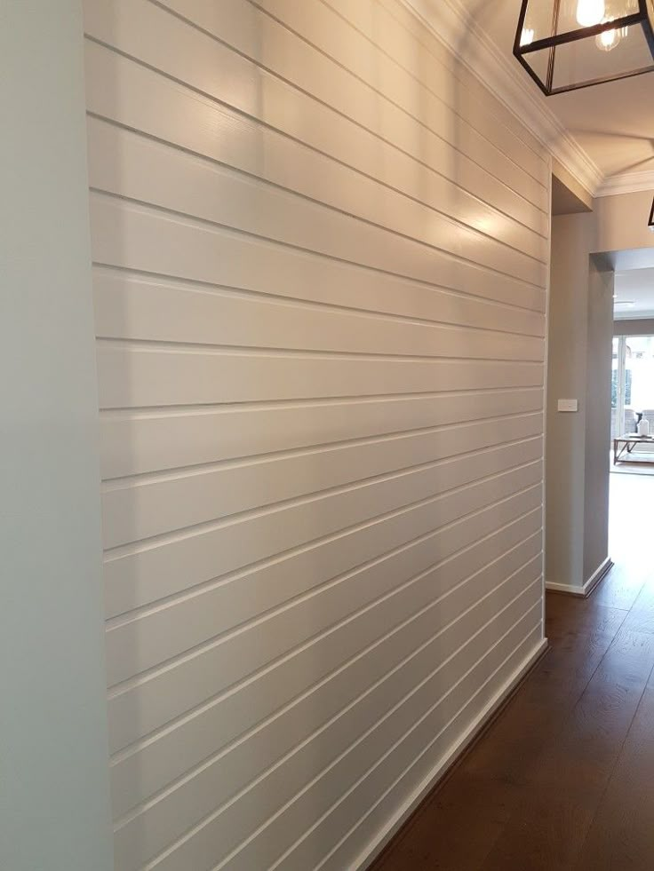 an empty hallway with white walls and wood flooring on either side is a light fixture hanging from the ceiling