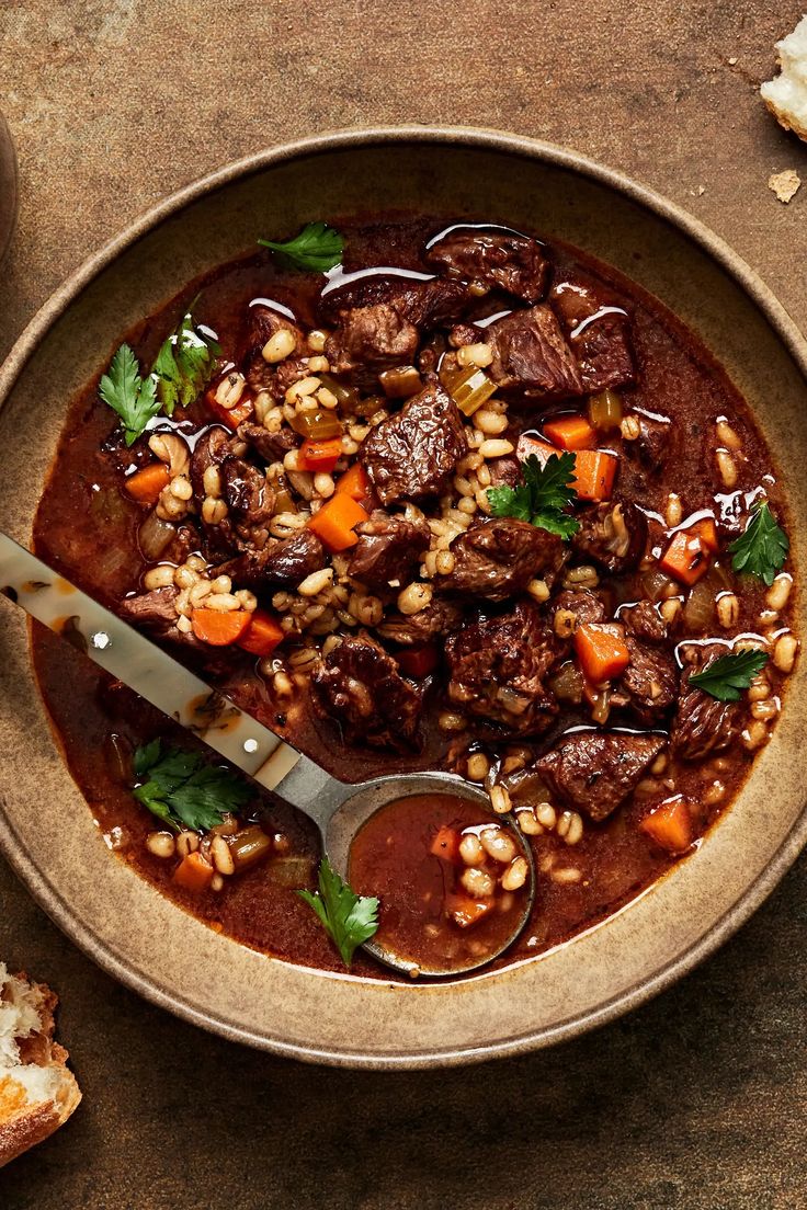 a bowl filled with meat, beans and carrots on top of a wooden table