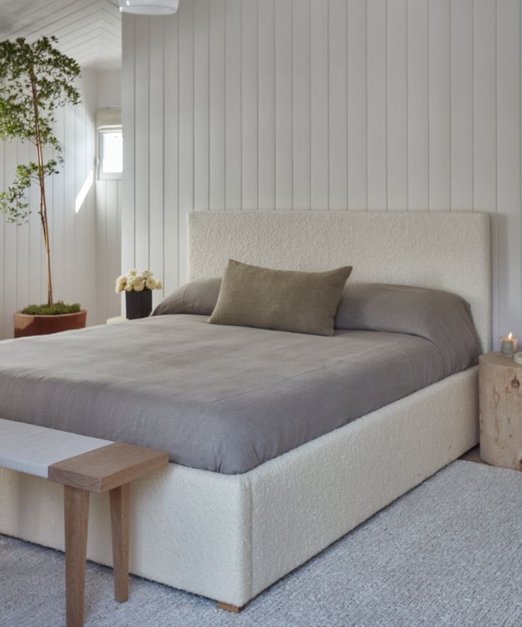 a large bed sitting next to a wooden table with a plant on top of it