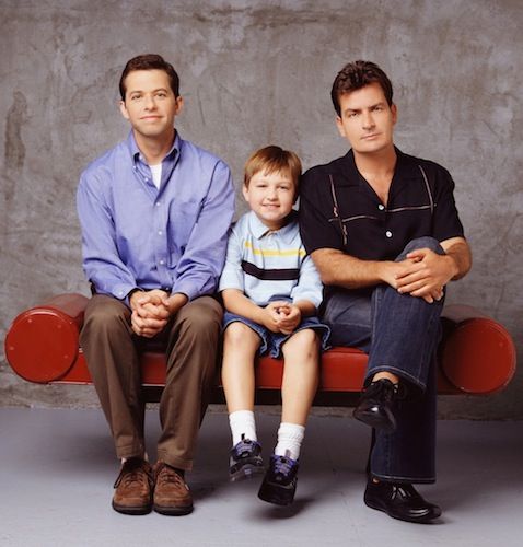 two men and a little boy sitting on a red bench in front of a cement wall