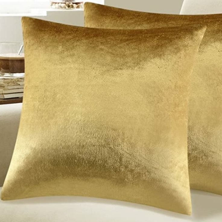 two gold pillows sitting on top of a bed next to a white pillowcase and table