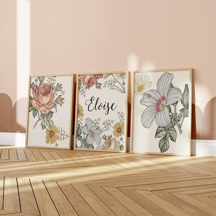 three framed flowers are on the floor in an empty room with pink walls and wooden floors