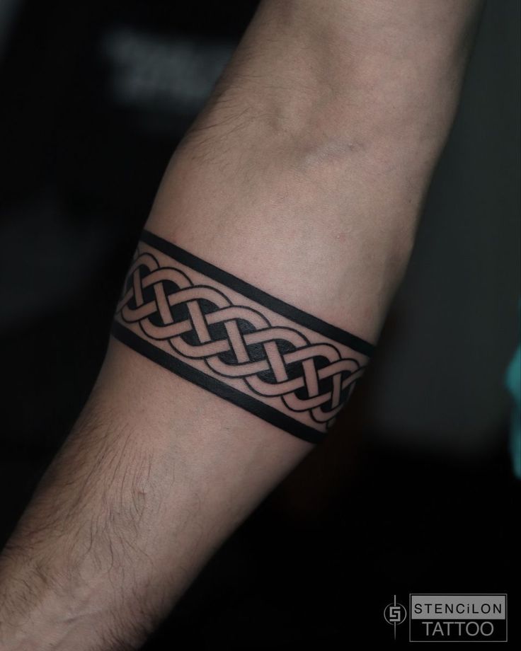 a man with a tattoo on his arm wearing a black leather bracelet that has an intertwined design