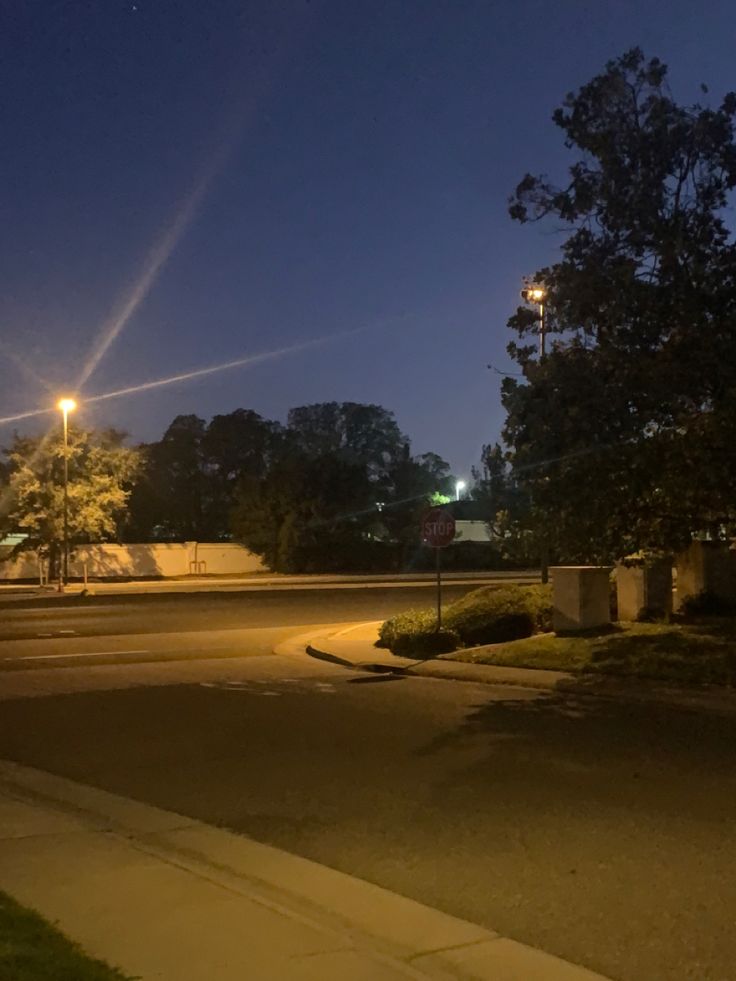 an empty street at night with the lights on and trees in the foreground,