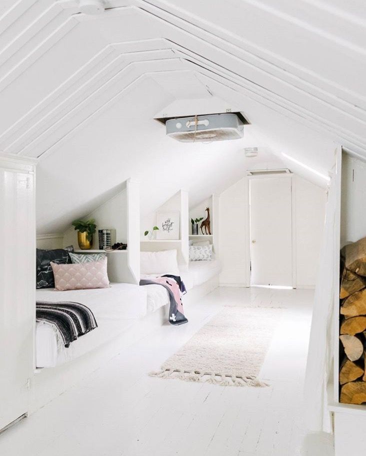 an attic bedroom with white walls and wood stacked on the floor in front of it