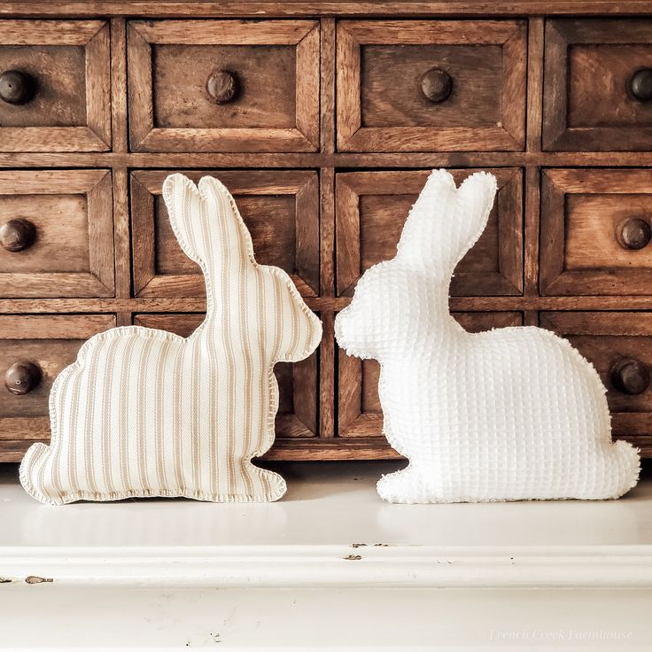 two knitted rabbits sitting next to each other in front of a dresser with text overlay