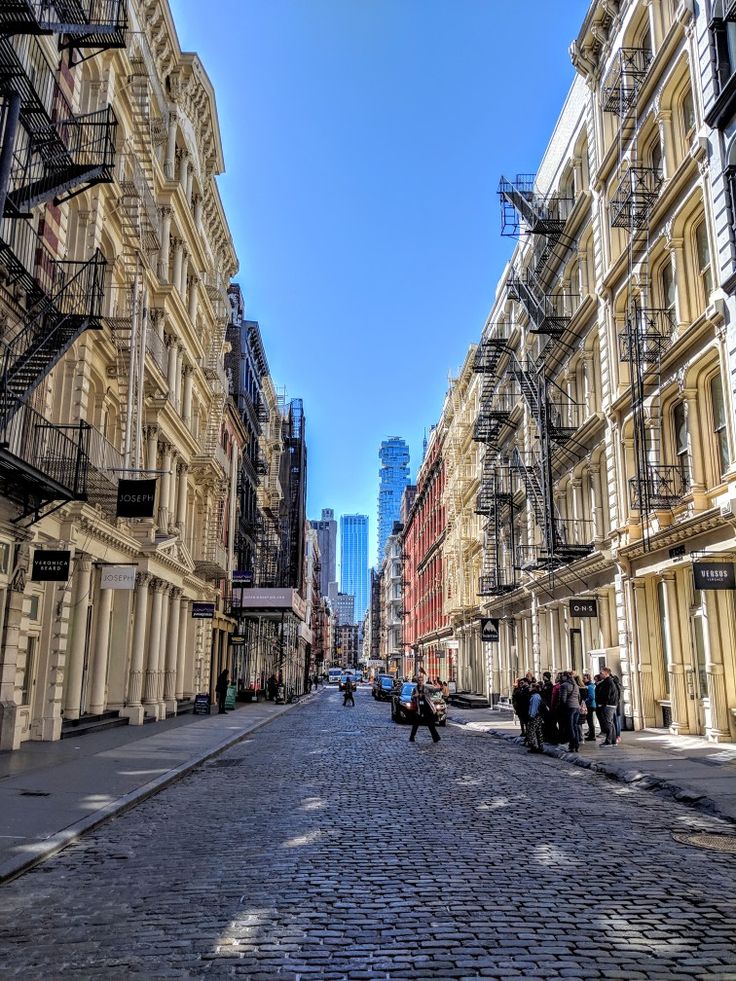 the people are walking down the cobblestone street in front of some tall buildings