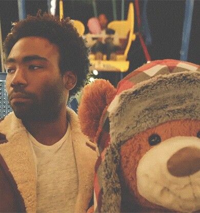 a man standing next to a teddy bear wearing a hat and coat at an amusement park