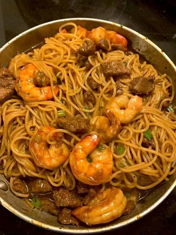 a pan filled with pasta and shrimp on top of a stove burner, ready to be cooked