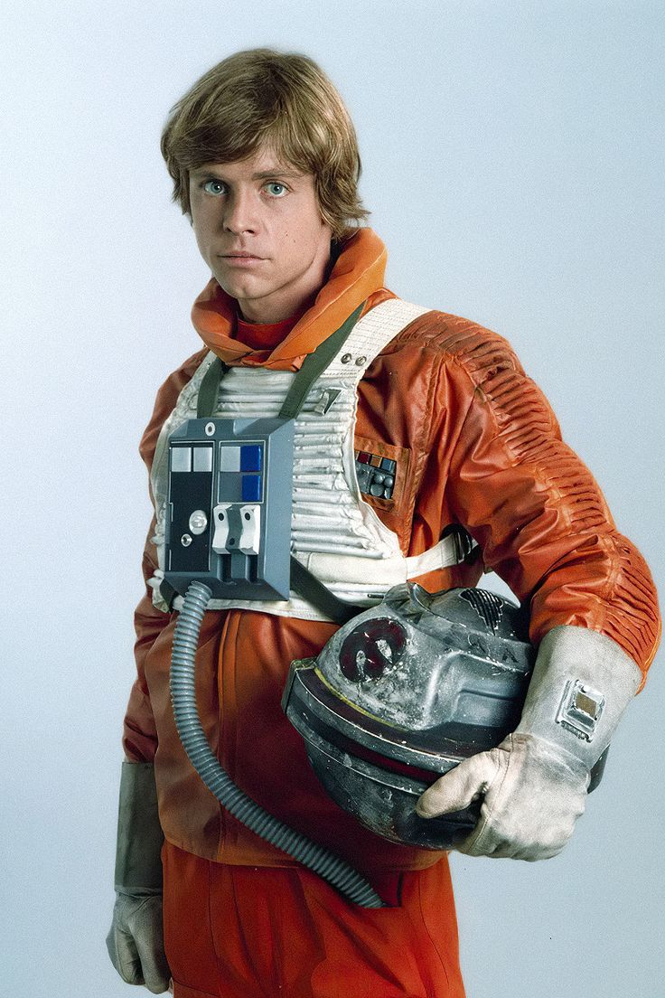 a man dressed in an orange space suit holding a helmet on his shoulder and looking at the camera