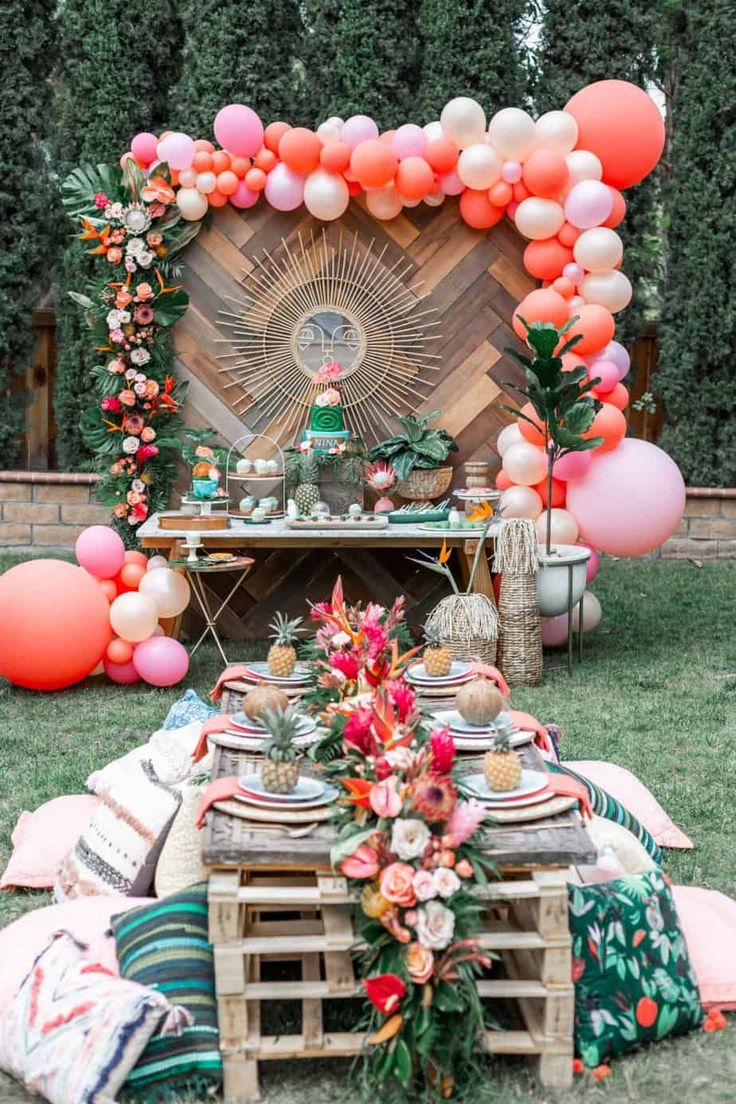 an outdoor table set up with balloons, plates and fruit on it for a party