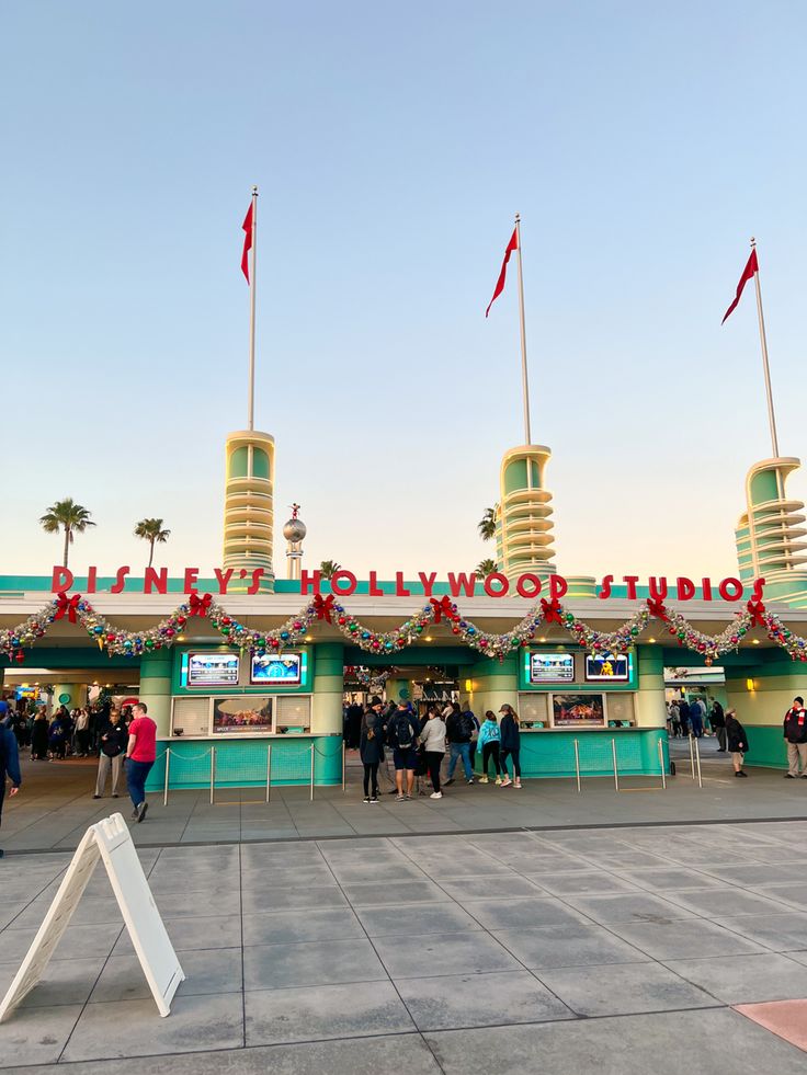 people are standing in front of the hollywood studios entrance at sunset or sunrise, with red and green flags flying above them