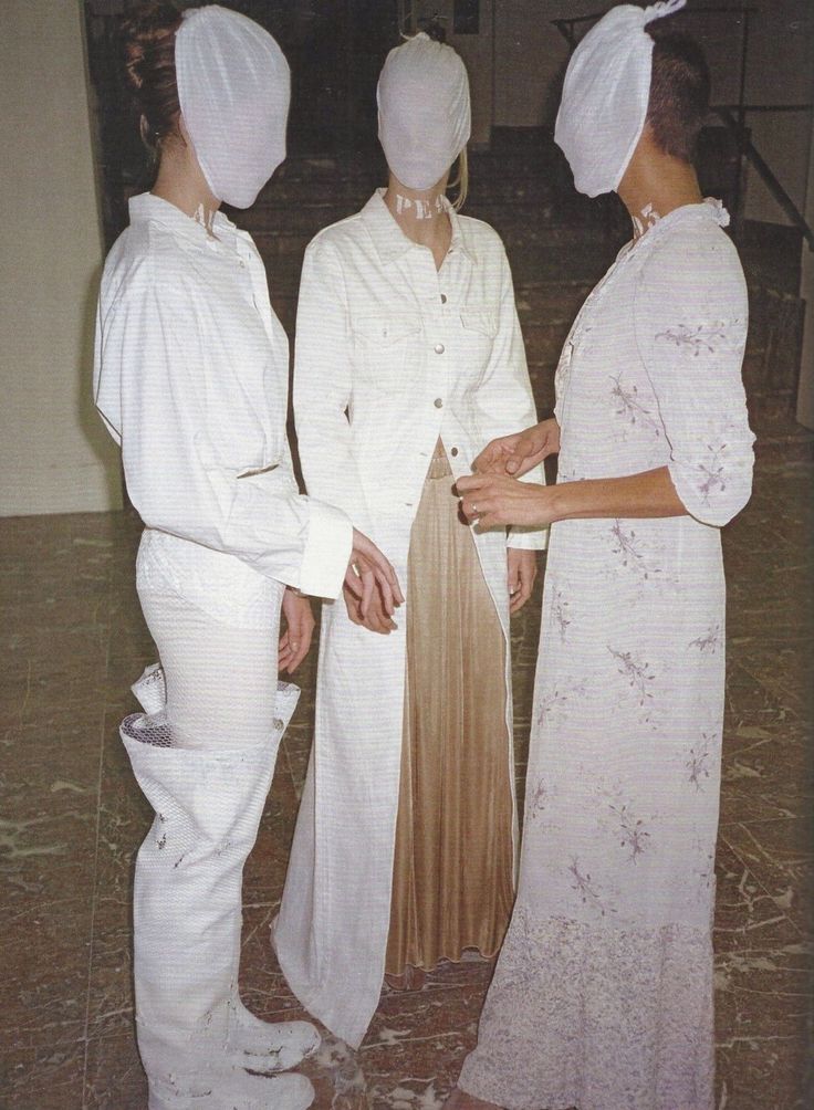 three people standing next to each other in front of a door wearing white clothing and bonnets