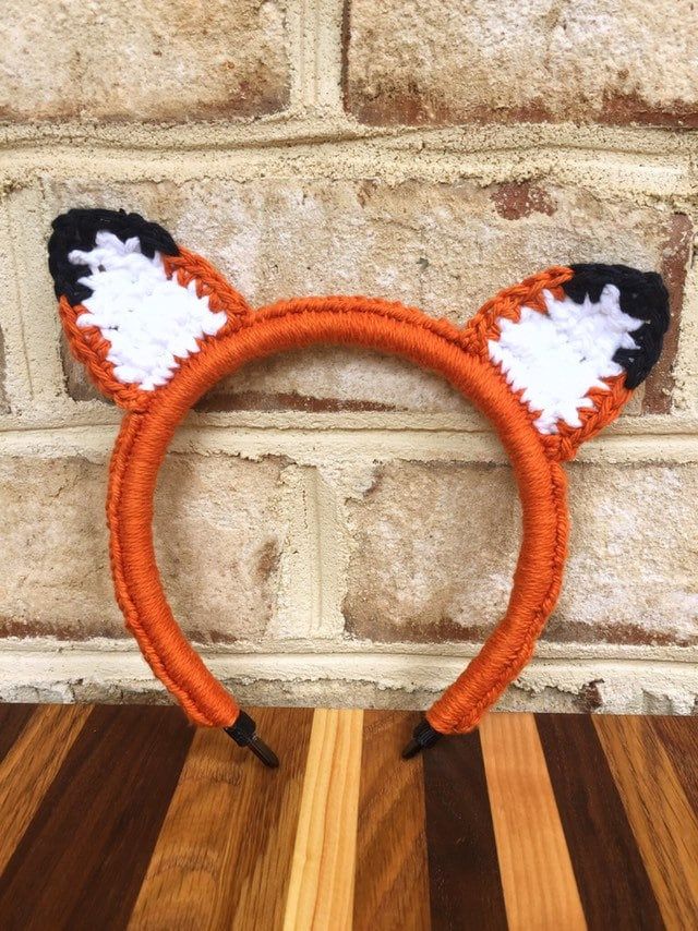 an orange and black cat ears headband on top of a wooden table next to a brick wall