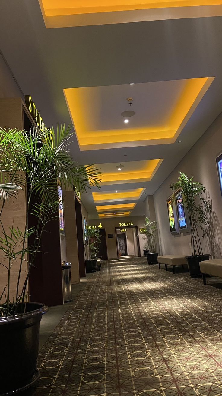 a long hallway with plants and televisions on the wall in it's center