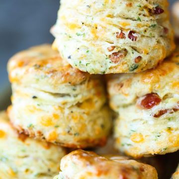 several biscuits stacked on top of each other in a metal pan with cheese and bacon toppings