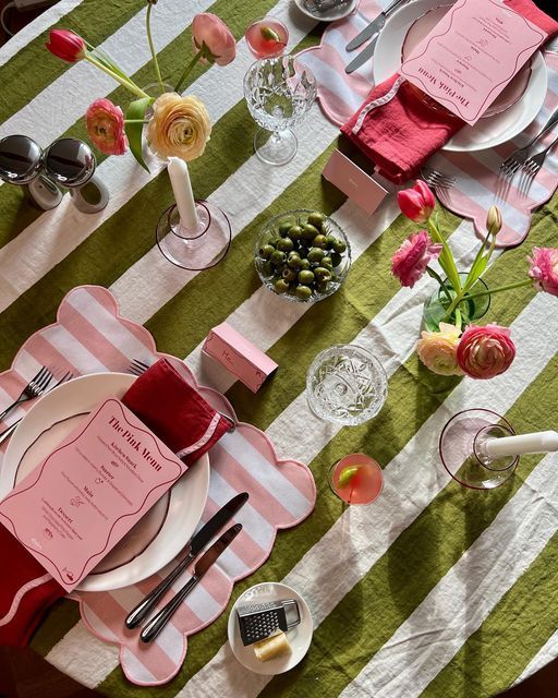 the table is set with pink and green place settings, silverware, napkins, and flowers