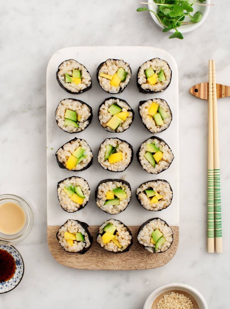 sushi rolls with mango and avocado on a white plate next to chopsticks