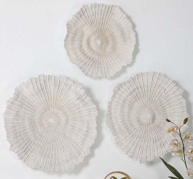 three white wicker plates on a table next to a vase with flowers in it